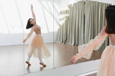 Genç balerin dans stüdyosundaki aynanın önünde dans tekniklerini ve zarafetini mükemmelleştiriyor.