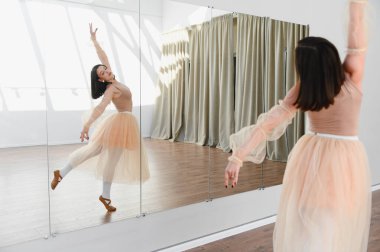 Genç balerin dans stüdyosunda bale çalışıyor. Tekniğini geliştirmek için ayna kullanıyor.