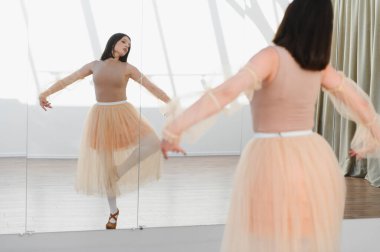 Genç balerin dans stüdyosundaki aynanın önünde dans figürleri yapıyor, etek ve sivri ayakkabılar giyiyor.