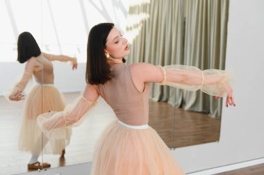 Genç balerin dans stüdyosunda zarif bale hareketleri yapıyor, etek ve şık kollarla süslenmiş, kendini işine adamış ve sanatını sergiliyor.