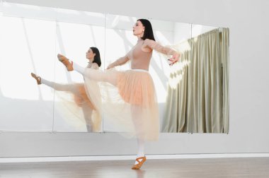 Genç bayan balerin bir dans stüdyosunda zariflik ve beceri sergileyerek aynanın önünde bacak uzatmak için alıştırma yapıyor.