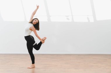 Ahşap zemin ve beyaz duvarları olan parlak bir stüdyoda çağdaş dans koreografisi uygulayan kadın dansçı.