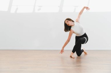 Dans öğrencisi ya da öğretmen, ahşap zemini ve doğal ışığı olan geniş bir stüdyoda modern dans figürü sergiliyor.