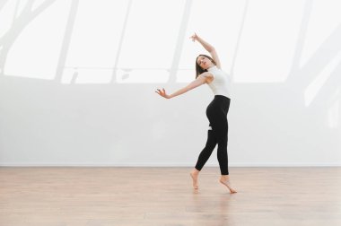 Parlak bir stüdyoda modern hareketler yapan zarif dansçı, esneklik ve sanatsal ifade sergiliyor.