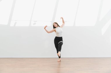 Geniş bir stüdyoda modern bir dans gösterisi sergileyen zarif dansçı esnekliğini ve sanatsal ifadesini sergiliyor.