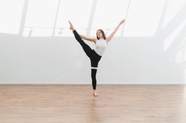 Dans öğrencisi, ahşap zemin ve beyaz duvarları olan parlak bir stüdyoda modern bir bale koreografisi uyguluyor.