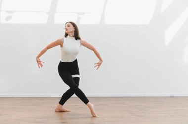 Modern bale koreografisini ahşap zemini ve beyaz duvarı olan parlak bir stüdyoda pratik yapan bir dans öğrencisi.