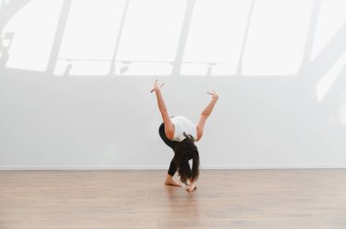 Parlak bir stüdyoda modern koreografi pratiği yapan kadın dansçı ahşap zeminde zarafet ve beceri sergiliyor.