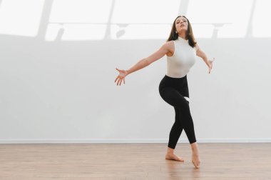 Dans öğrencisi ya da öğretmen parlak bir stüdyoda zarif bir modern dans gösterisi yapıyor. Esneklik ve sanatsal ifade sergiliyor.