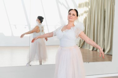 Bir dans stüdyosunda bale antrenmanı yapan, beyaz tayt ve pembe etek giyen zarif ve tutkulu bir balerin.