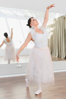 Yaşlı balerin akıcı beyaz bir elbiseyle zarif bir şekilde dans ediyor, stüdyo aynasında çarpıcı bir yansıma yaratıyor, zarafet ve sanatın vücut bulmuş hali.