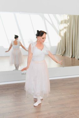 Yaşlı balerin zarif bir şekilde dans stüdyosunda bale adımları atar, arka plandaki zarif hareketlerini yansıtır.