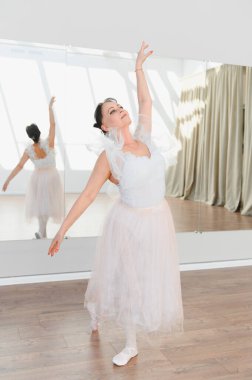 Yaşlı balerin zarif bir şekilde beyaz bir elbise ve bale ayakkabılarıyla dans eder. Yansıması dans stüdyosundaki hareketlerini yansıtır.