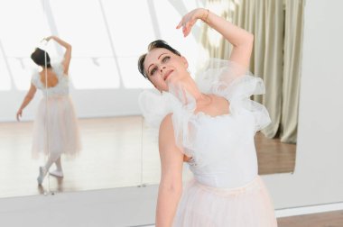 Zarif üst düzey balerin, parlak bir dans stüdyosunda dans figürleri yapıyor. Yansıması, zarafetini ve sanatına olan bağlılığını yansıtıyor.