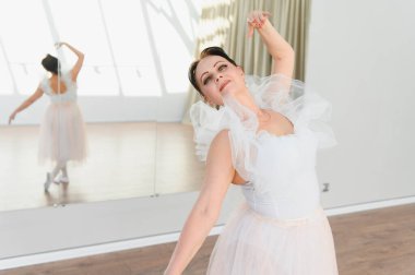 Yaşlı balerin dans stüdyosunda bale hareketleri yapıyor. Yansıması büyük bir aynada görülüyor.