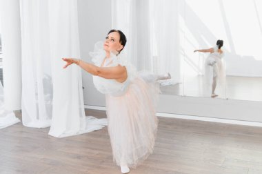 Yaşlı balerin bir dans stüdyosunda bale yapıyor, beyaz ve pembe etek giyiyor, dans için zarafet ve tutku gösteriyor.