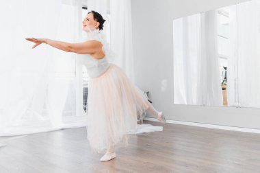 Yaşlı balerin nazikçe kolunu ve bacağını uzatır ve ayna ile parlak bir stüdyoda dans eder.