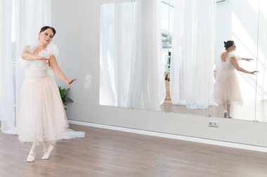 Yaşlı balerin bir dans stüdyosunda bale hareketleri yapıyor, yansıması büyük bir aynada görünüyor, sanatına olan bağlılığını ve zarafetini gösteriyor.