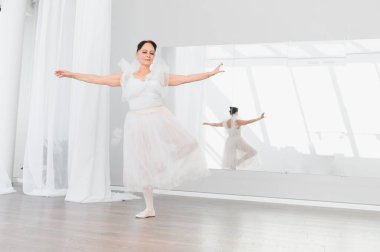 Zarif üst düzey balerin bale hareketleri yapıyor, zarif ve kendini dans etmeye adamış bir şekilde parlak bir stüdyoda dans ediyor.