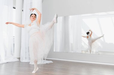 Zarif yaşlı balerin büyük bir aynaya yansıyan parlak bir stüdyoda bale hareketleri yapıyor.