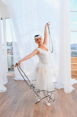 Yaşlı balerin parlak bir stüdyoda zarif bir dans gösterisi yapıyor, beyaz bir elbise ve tüylü bir başlık giyiyor, zarafet ve bale tutkusu sergiliyor.