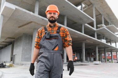 Güvenlik üniformalı ve kasklı bir bina, bitmemiş beton bir yapının önünde duruyor, gelişimi temsil ediyor.