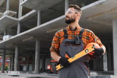İnşaat işçisi inşaat alanında duruyor, başlık takıyor, güvenlik gözlüğü takıyor ve üniforma giyiyor.