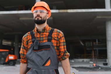 İnşaat işçisi, inşaat alanında şapka ve güvenlik gözlüğü takıyor, odaklanmış ve profesyonel, projeyi yönetmeye hazır.