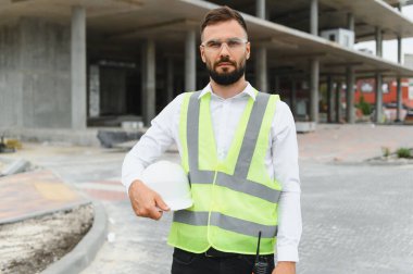 Erkek inşaat işçisi, güvenlik yeleği ve şapka takıyor, inşaat projesini denetliyor. İş sahasında profesyonel mühendis