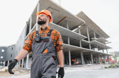 Başlık ve güvenlik gözlüğü takan inşaatçı, modern bir ticari bina inşaatında ilerlemeyi denetliyor.