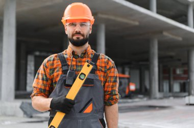 Güvenlik teçhizatında inşaat işçisi, ruhsal bir seviyede, endüstriyel inşaat alanında duruyor.
