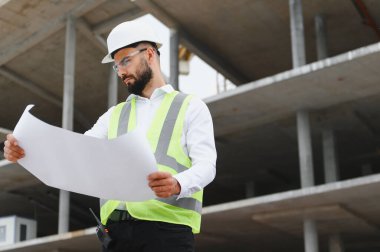Profesyonel inşaat işçisi veya mühendis bina planlarını gözden geçirir, ticari kalkınma sürecini denetler