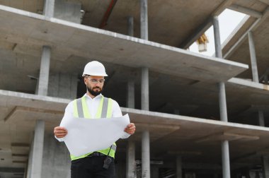 İnşaat alanında inşaat başlığı ve güvenlik yeleği giyen bir mühendis. Yapı süreci denetleniyor
