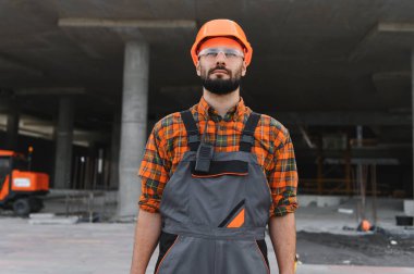 İnşaat alanında güvenlik teçhizatıyla çalışan bir işçi, kameraya ciddi ciddi bakıyor. Sıkı çalışma ve güvenliği temsil eder.