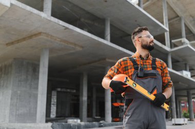 Güvenlik gözlüğü ve tulum takan yetenekli inşaat işçisi inşaat sahasında baret ve ruh seviyesi tutuyor.