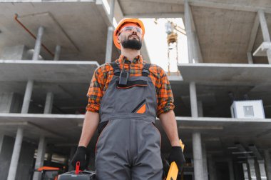 Güvenlik teçhizatlı bir adam, inşaat ve geliştirme aşamasındaki beton bir binaya bakıyor.