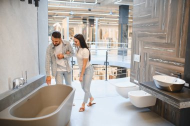 Genç bir çift banyo küveti seçiyor, banyo yenileme alışverişinde ürün kalitesini kontrol ediyorlar.
