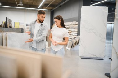 Adam hırdavatçıda kadına fayans örneği sunuyor, yeni ev döşeme projeleri için kararlar alıyor.