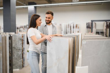 Genç bir çift, bir hırdavatçıda döşeme ve duvar döşemelerini karşılaştırıyor. Ev yenileme projelerini birlikte planlıyorlar.