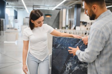 Mavi mermer seçen genç çift, bir ev geliştirme mağazasında fayanslara bakıyor, bir banyo veya mutfak yenileme planı yapıyorlar.