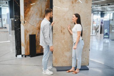 Genç bir çift modern bir tasarım galerisinde mermer döşemelerin yenilenmesi için bakıyor, tartışıyor ve seçiyor.