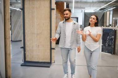 Genç çift sergi salonunda yürürken ev geliştirme seçeneklerini tartışıyor. Yeni döşeme ve banyo tadilatı planlıyorum.