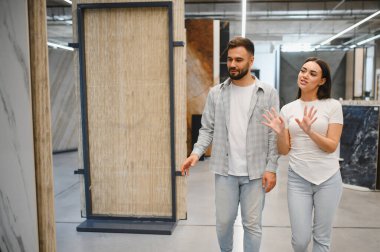 Geniş bir hırdavat dükkanındaki örnek fayanslara bakan genç bir çift, ev geliştirme projeleri için malzeme seçiyorlar.