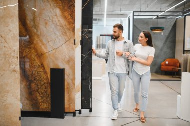 Modern bir galeride yürüyen genç çift, ev yenileme için doğal taşlara ve granit plakalara dokunuyor ve onları seçiyor.