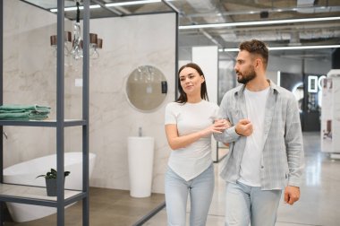 Genç bir çift, yeni banyo tesisatı ve tasarım fikirlerini seçerek bir ev geliştirme mağazasında yürüyor.