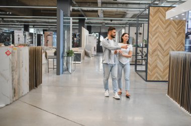 Sergi salonunu keşfeden genç bir çift, yeni fayanslar seçiyor ve ev dekorasyonu için döşeme yapıyor, tasarım kararlarını birlikte tartışıyorlar.