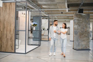 Fayans ve döşeme sergisi gezen genç bir çift, ev geliştirme ve yenileme projelerinin seçeneklerini tartışıyor.