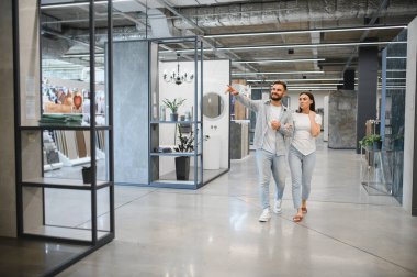 Mutlu çift modern sergi odalarını ve döşemeleri geziyor, insanlar gülümserken örneklere bakıyor ve evlerini birlikte yenilemeyi planlıyorlar.