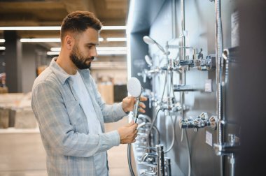 Hırdavatçıda modern duş başlıklarını karşılaştıran bir adam, bir ev yenileme projesi ve tesisat yenileme için banyo malzemeleri seçen bir adam.