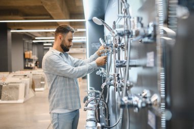 Modern bir ev geliştirme mağazasında farklı duş sistemlerini ve muslukları inceleyen adam banyo güncellemelerini planlıyor.